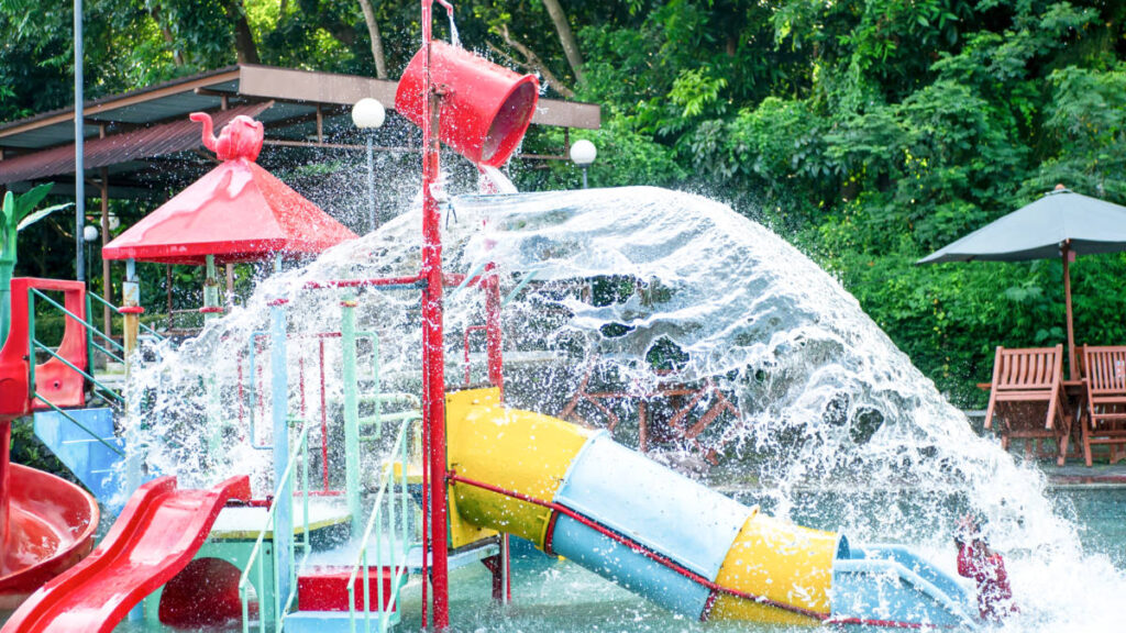 A red bucket pouring water over the slide in the mini waterpark