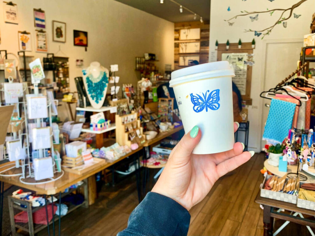 A hand holding a coffee cup with blue butterfly inside the Mission Blue Butterfly