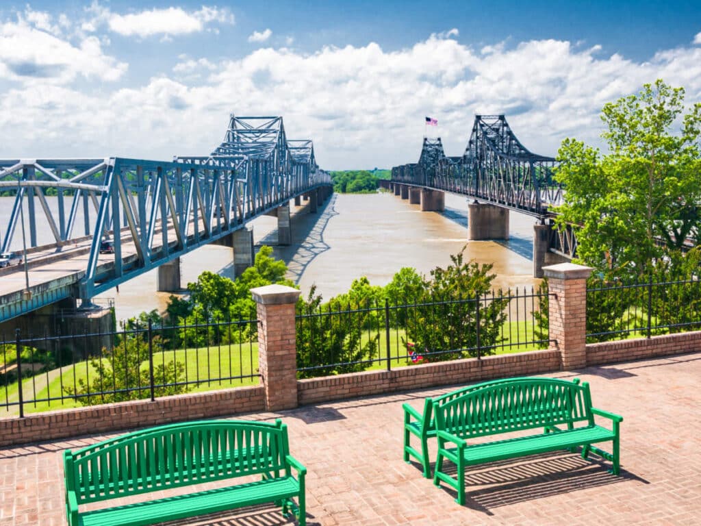 Two green benches with the Mississippi River bridge in the background on a sunny day