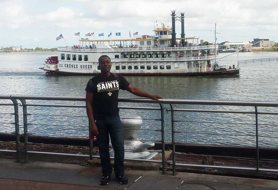 The author posing for a photo with a ship on the Mississippi River at the background