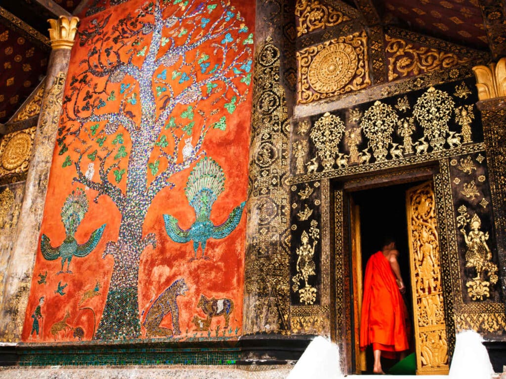 A monk walking inside the intricate Wat Xiengthong