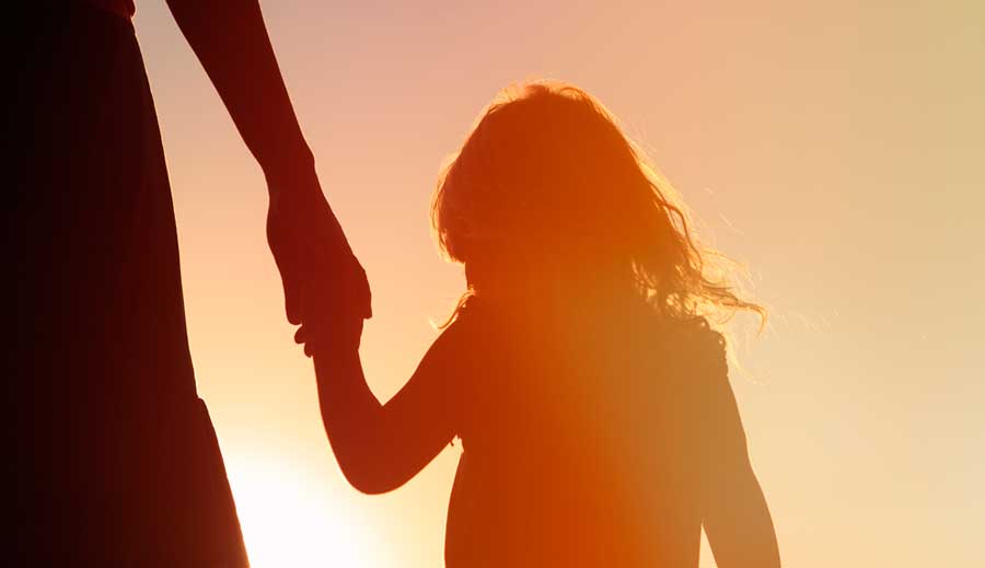 A silhouette of a woman holding her daughter's hand during sunset