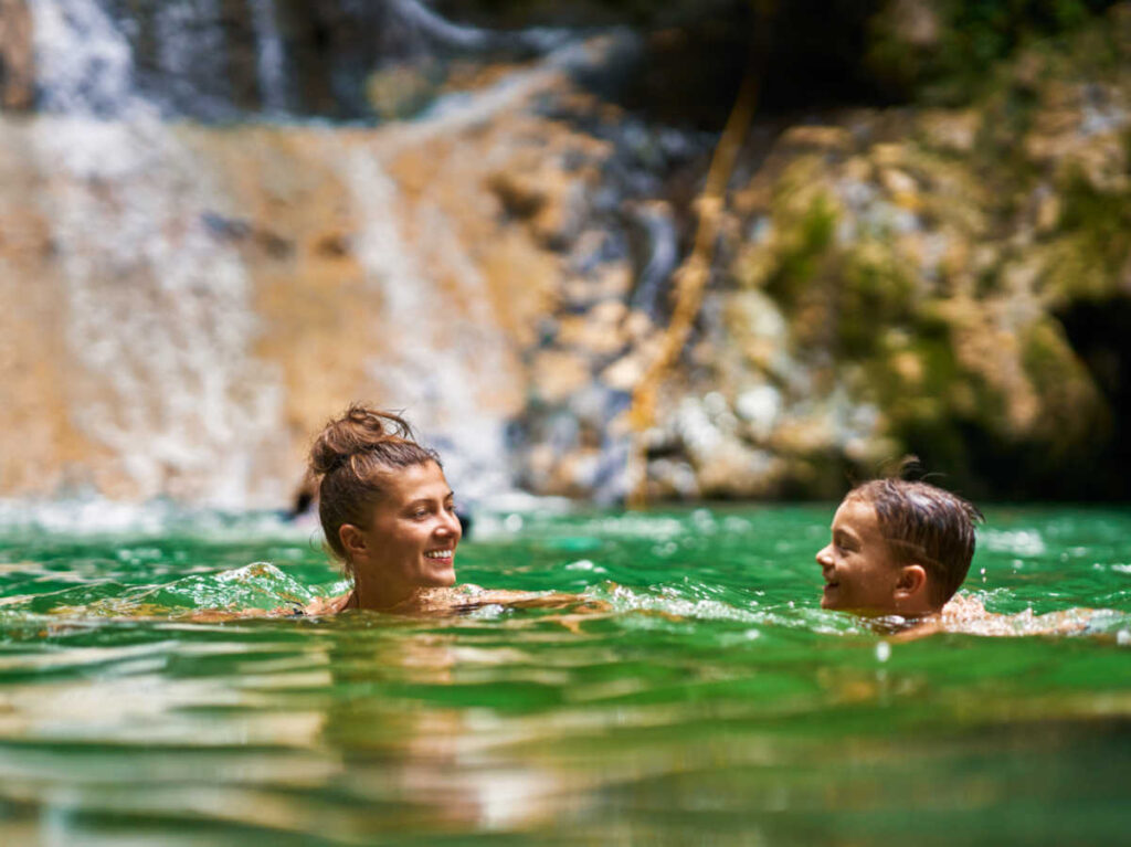 A mother and son swimming near the waterfalls