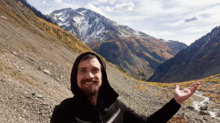 The author Matthew Reppond, posing for a photo with the mountain valley in the background in Svaneti