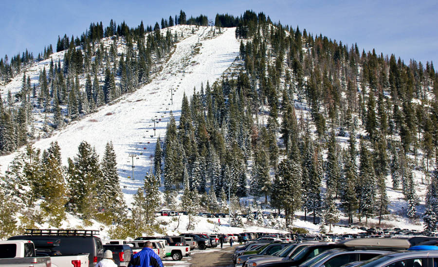 A snow covered mountain slope of Mt. Shasta Ski Park with a fully packed parking below.