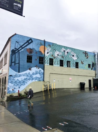 View of a man crossing by the mural on a building in downtown Tacoma on a rainy day