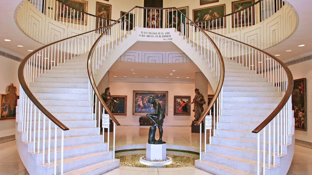 View of the grand staircase surrounded with wall paintings and a sculpture in the middle of Museo de Arte de Ponce
