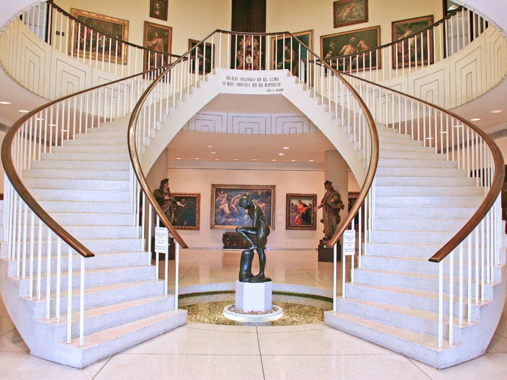 View of the grand staircase surrounded with wall paintings and a sculpture in the middle of Museo de Arte de Ponce