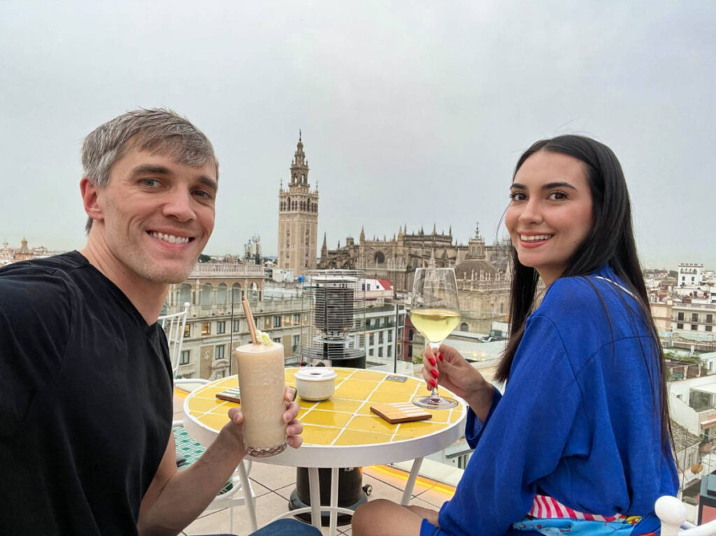 Travel Lemming Founder Nate and Clara, enjoying their drinks with an overlooking view at Querencia de Sevilla’s Rooftop Bar