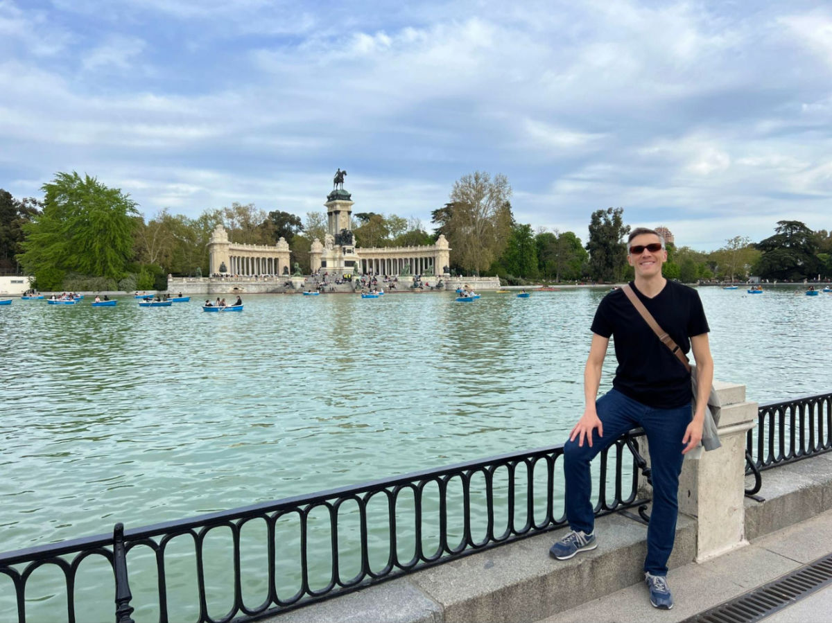 Travel Lemming founder Nate standing on a railing near a lake in Parque del Buen Retiro in Madrid