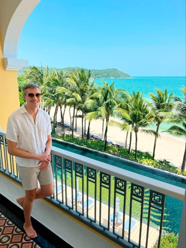 Nate smiling for a photo on the balcony of their room in JW Marriott Phu Quoc Emerald Bay Resort & Spa