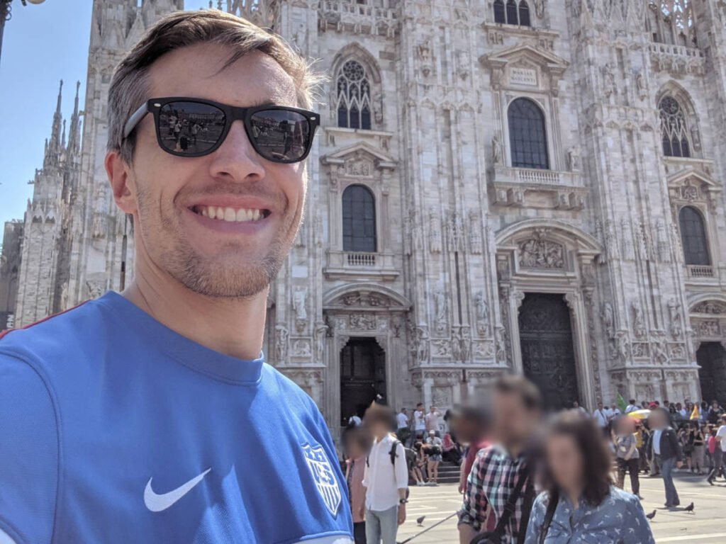 Travel Lemming Founder Nate Hake smiling for a photo while wearing his USA soccer jersey in Milan