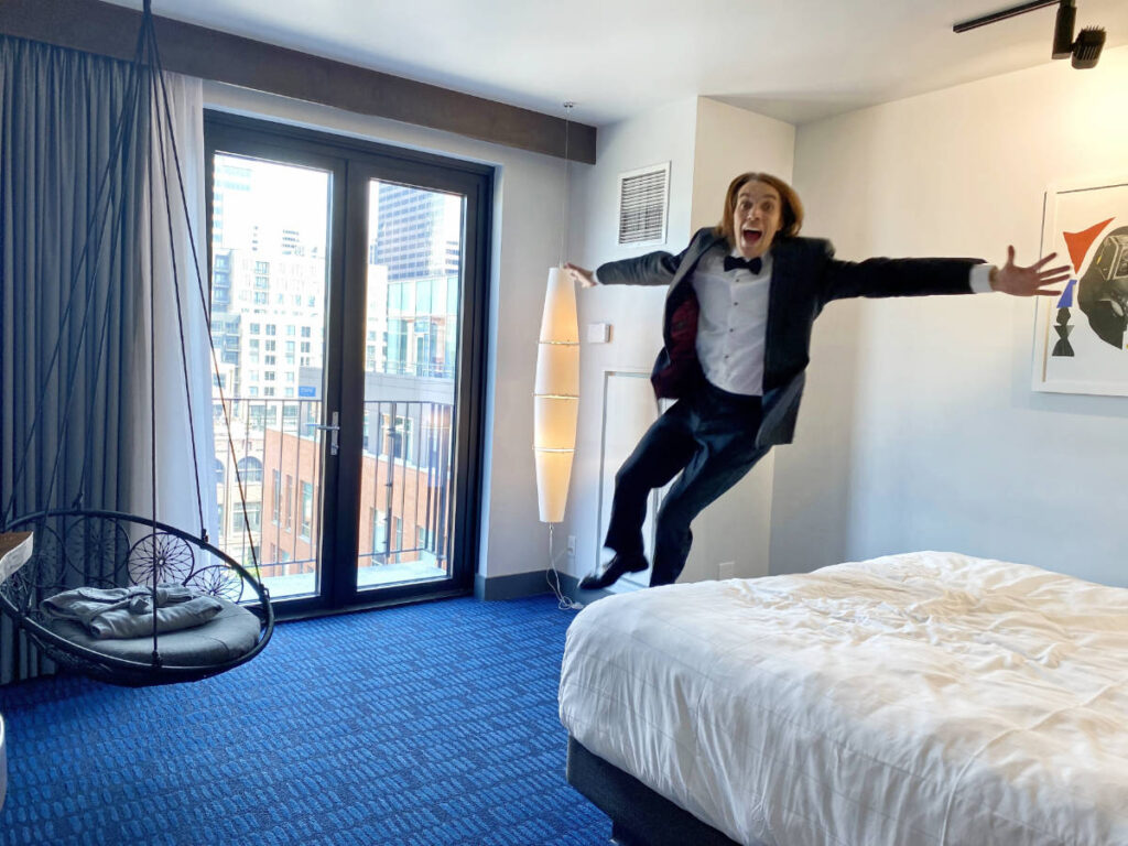 The author, Nate Hake jumping onto the bed in their room in The Maven Hotel