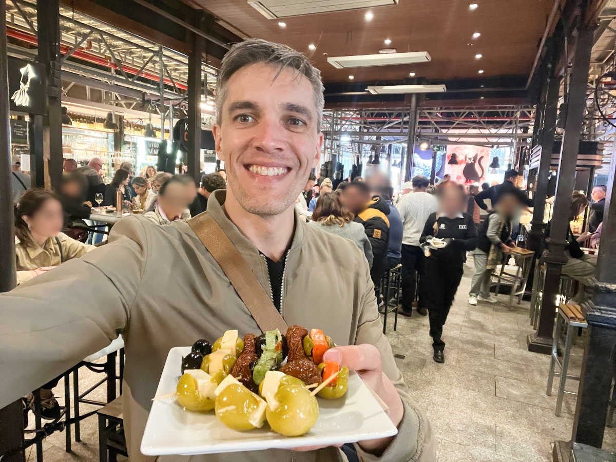 Travel Lemming’s founder Nate Hake holding a plate of snacks inside Mercado de San Miguel