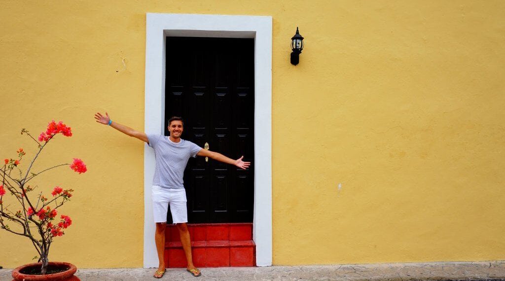Nate with arms outstretched against a colorful colonial wall
