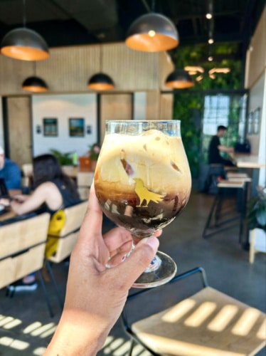 A hand holding a glass of N'awlins cold brew at Corvus Coffee Roasters