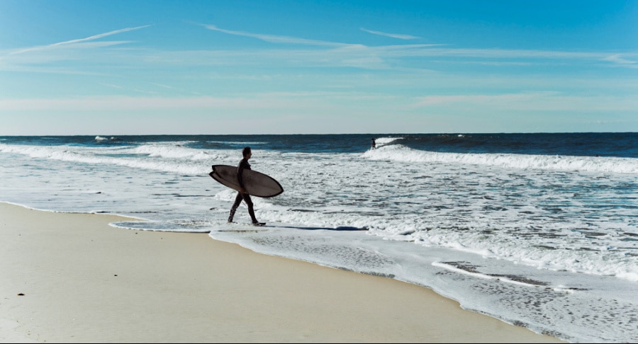 A surfer with a surfboard walking along the shore of Nazare's beach