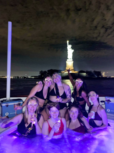 The author Niamh Hayes and her friends taking a photo on the hot tub at night with the Statue of Liberty in the background