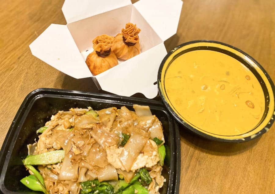 A bowl of curry sauce, a dish of noodles, and crunchy pouches in Nittaya's Little Kitchen