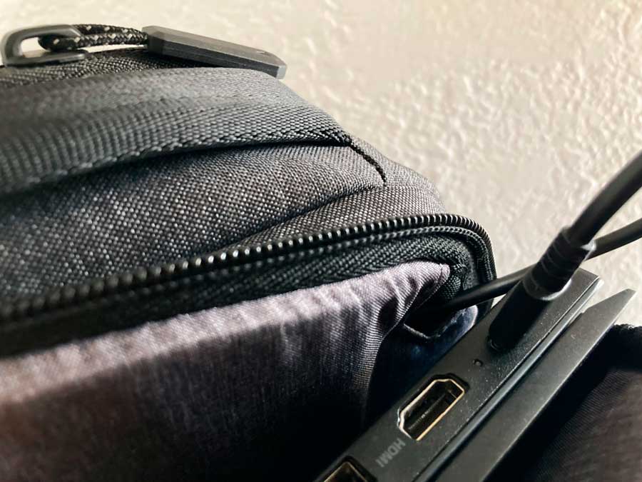 View of a laptop being charged on the charging cord slot of Nomatic Navigator Lite Backpack
