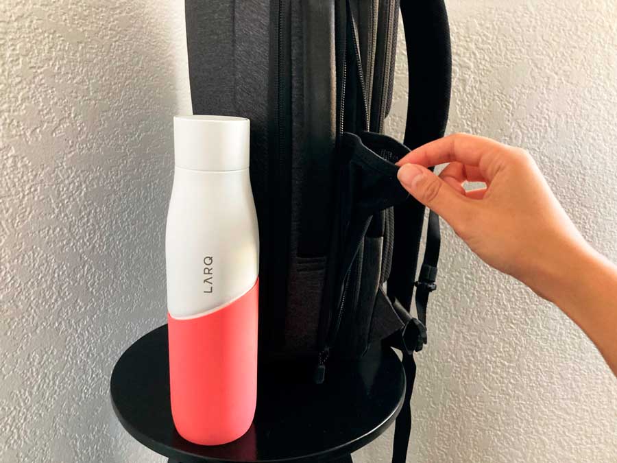 A water bottle and the Nomatic Navigator Lite Backpack on a chair