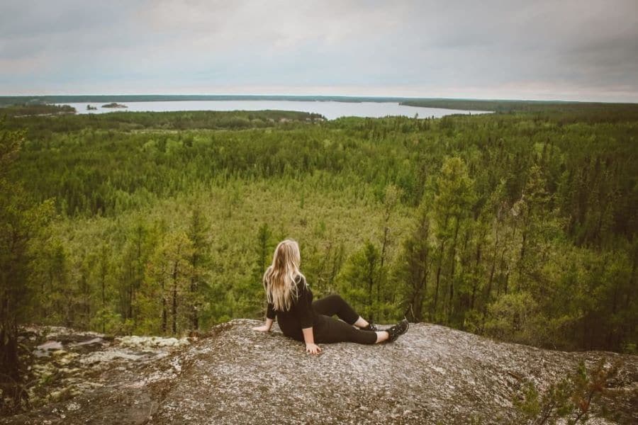 Taylor sits on a rocky cliff overlooking the forest and lakes of Nopiming Provincial Park