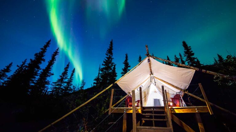 View of the glowing Northern lights glowing in the night sky of Alaska with a tent in the foreground