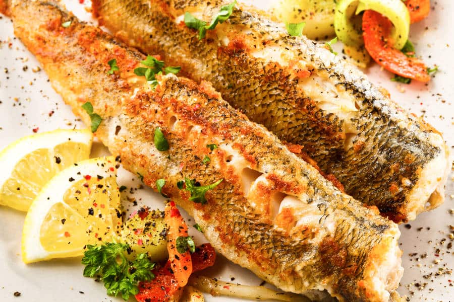 A dish of two fried fishes with vegetables around