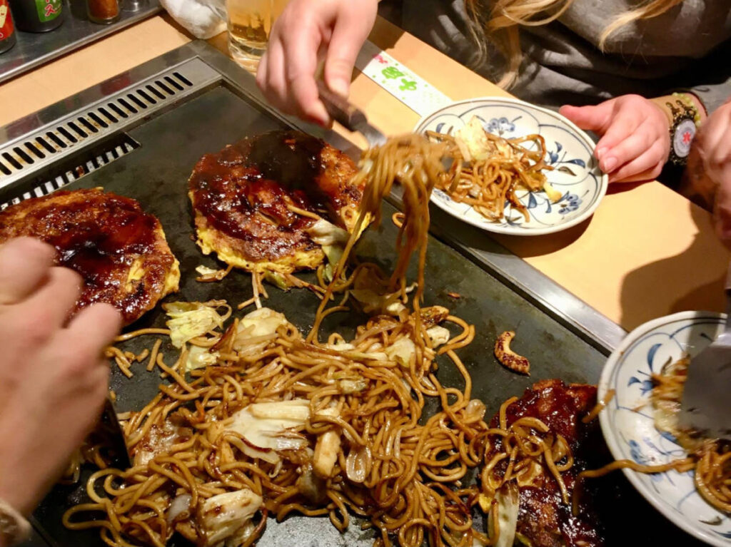 People eating okonomiyaki and yakisoba noodles
