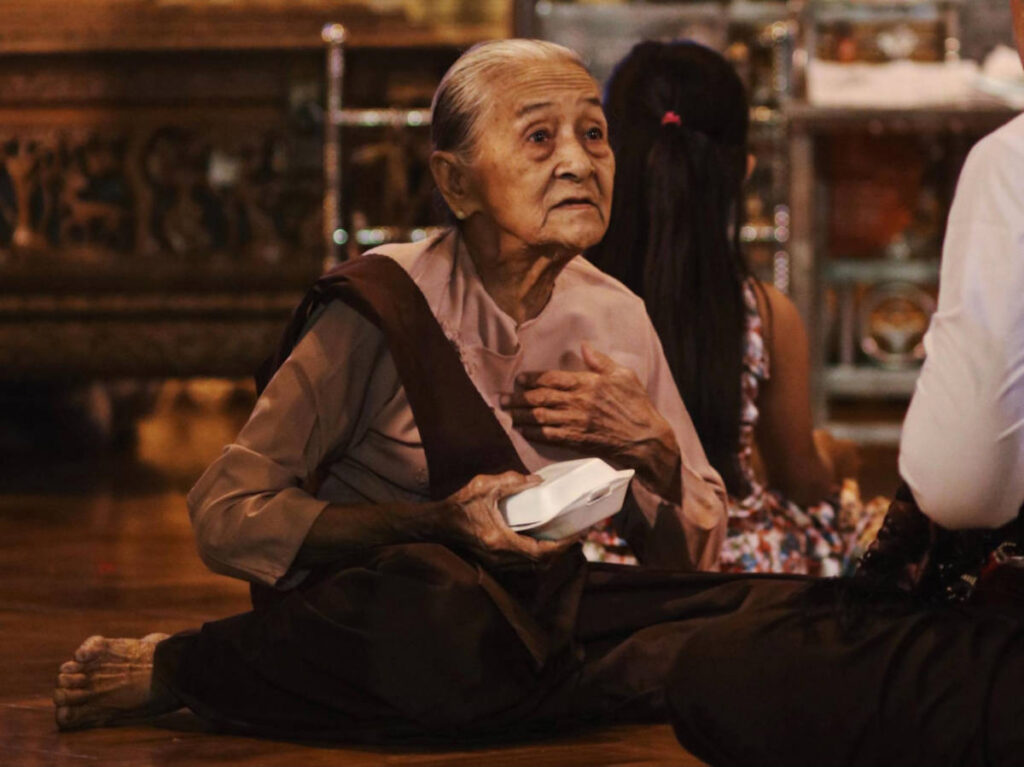 An elderly woman sitting on the floor inside the Shwedagon Pagoda