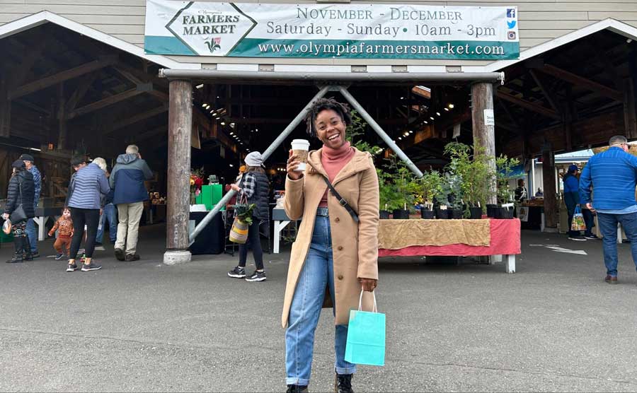 Author Chelsea holding a cup of coffee in front of Olympia Farmers Market