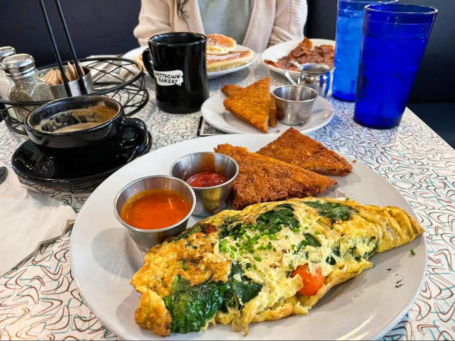 A plate of omelet filled with vegetables, hash browns and two small bowls of sauces on the side