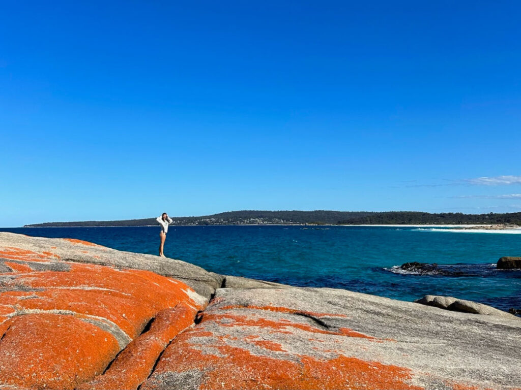 Author Laura standing on the orange-covered rocks at the Bay of Fires