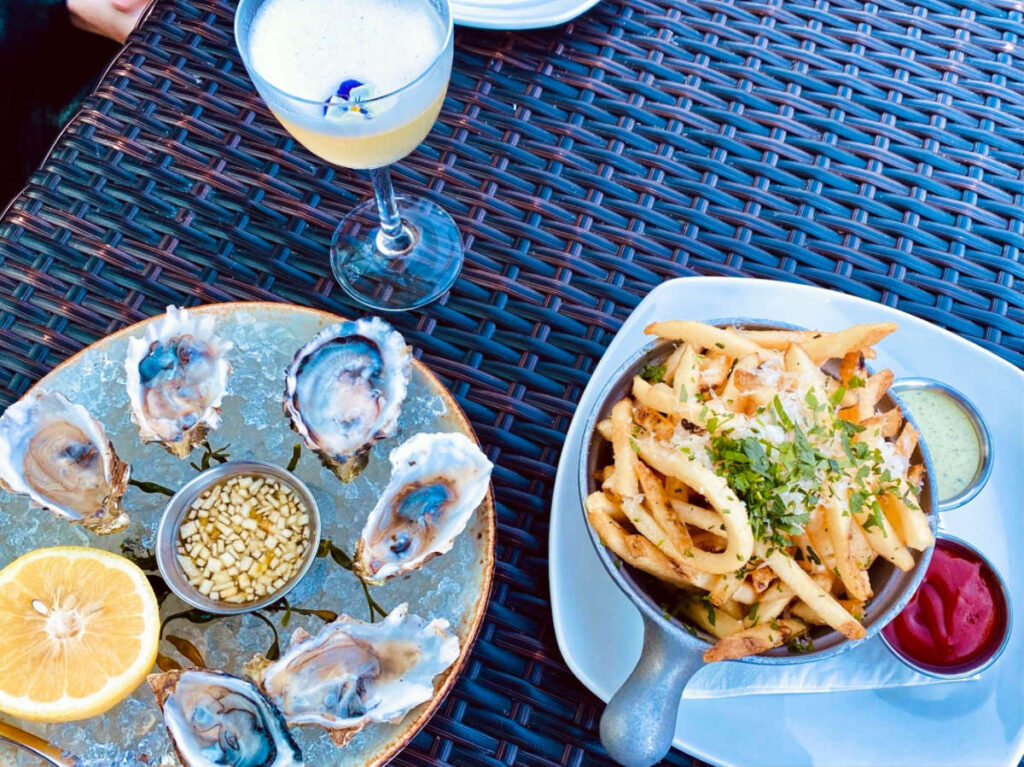 A plate of fresh oysters with lemon and a plate of fries with dipping sauce