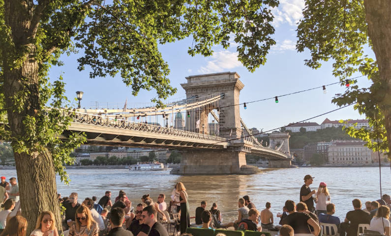 View of the Chain Bridge in Budapest with a crowd at Pontoon bar in the foreground