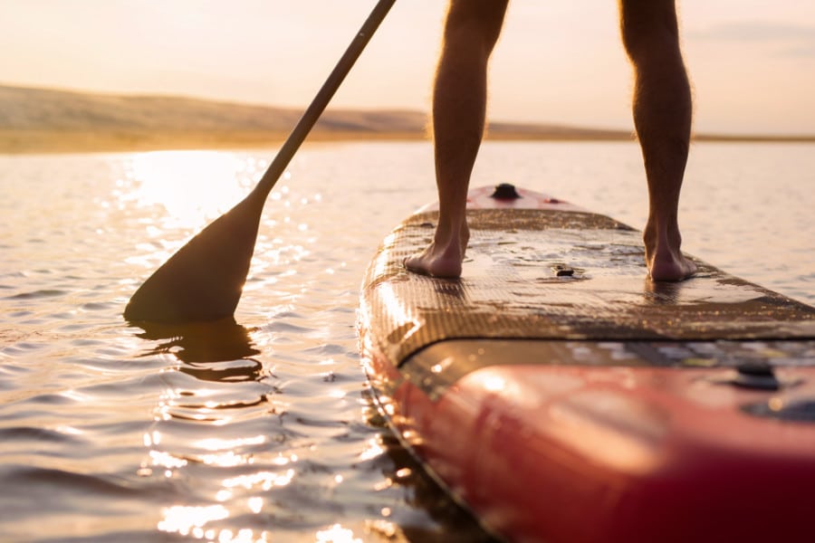 View of a man's feet riding a paddleboard on the lake at sunset