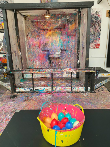 Colorful eggs in a bucket on a table, placed in front of a painting at Studio Interactive showcasing paintball art