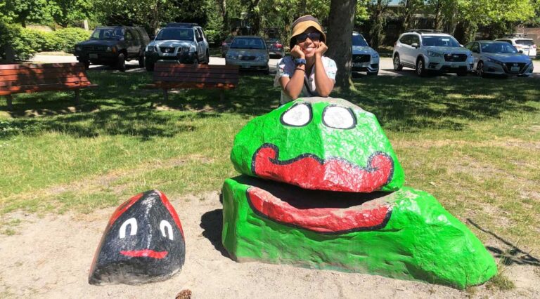 The author Chelsea Booker posing for a photo with painted rocks in Bainbridge Island