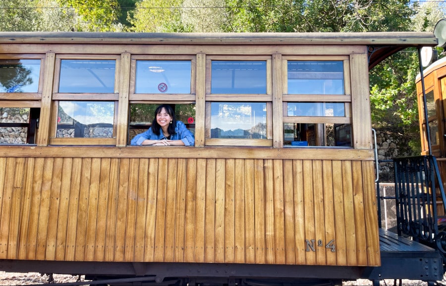 The author Lea Rose Allbaugh posing by the small window of a vintage tram in Soller