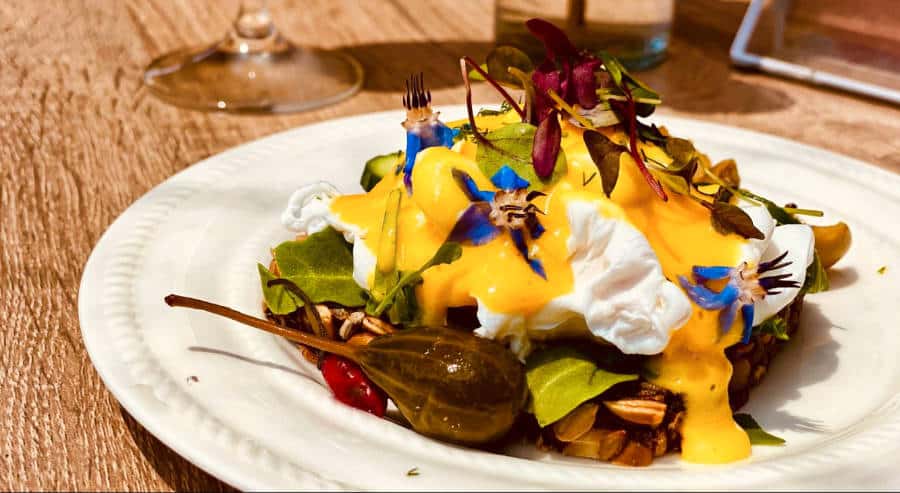 A plate of poach egg toast with capers, hollandaise sauce and edible flowers