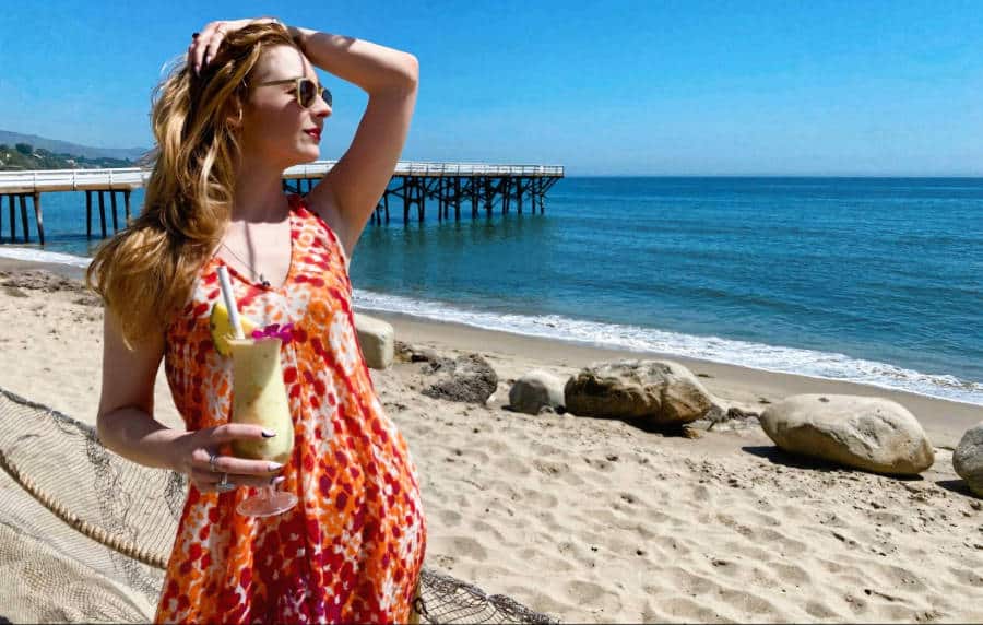 A woman posing at the shoreline while holding a drink with boardwalk at the background at Paradise Cove