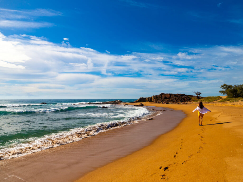 Woman in white shirt walking along paradise beach in Deepwater National Park near Agnes Water, Queensland