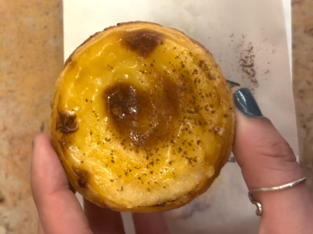 Holding a Cinnamon-dusted pastel de nata from Manteigaria