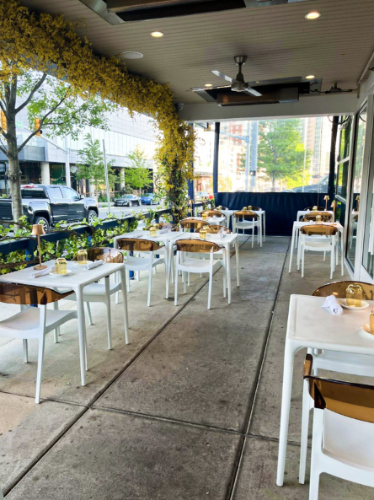 The outdoor dining setup with tables and chairs near the sidewalk at the patio of Luogo