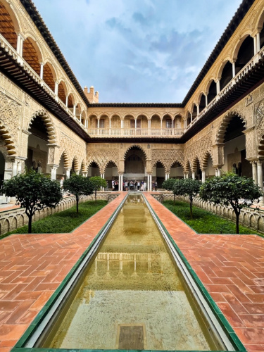 People tour around the Royal Alcazar with a long pool surrounded by pathways and beautiful arches