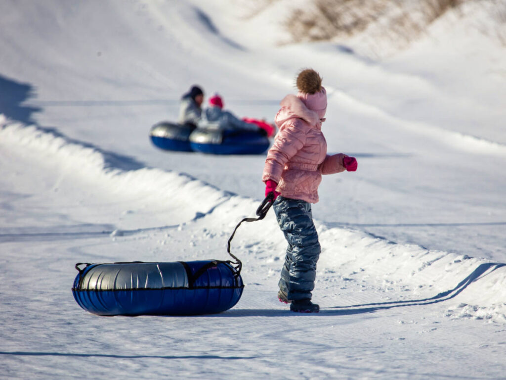 A child holding down the snow tube with other people snow tubing in the background