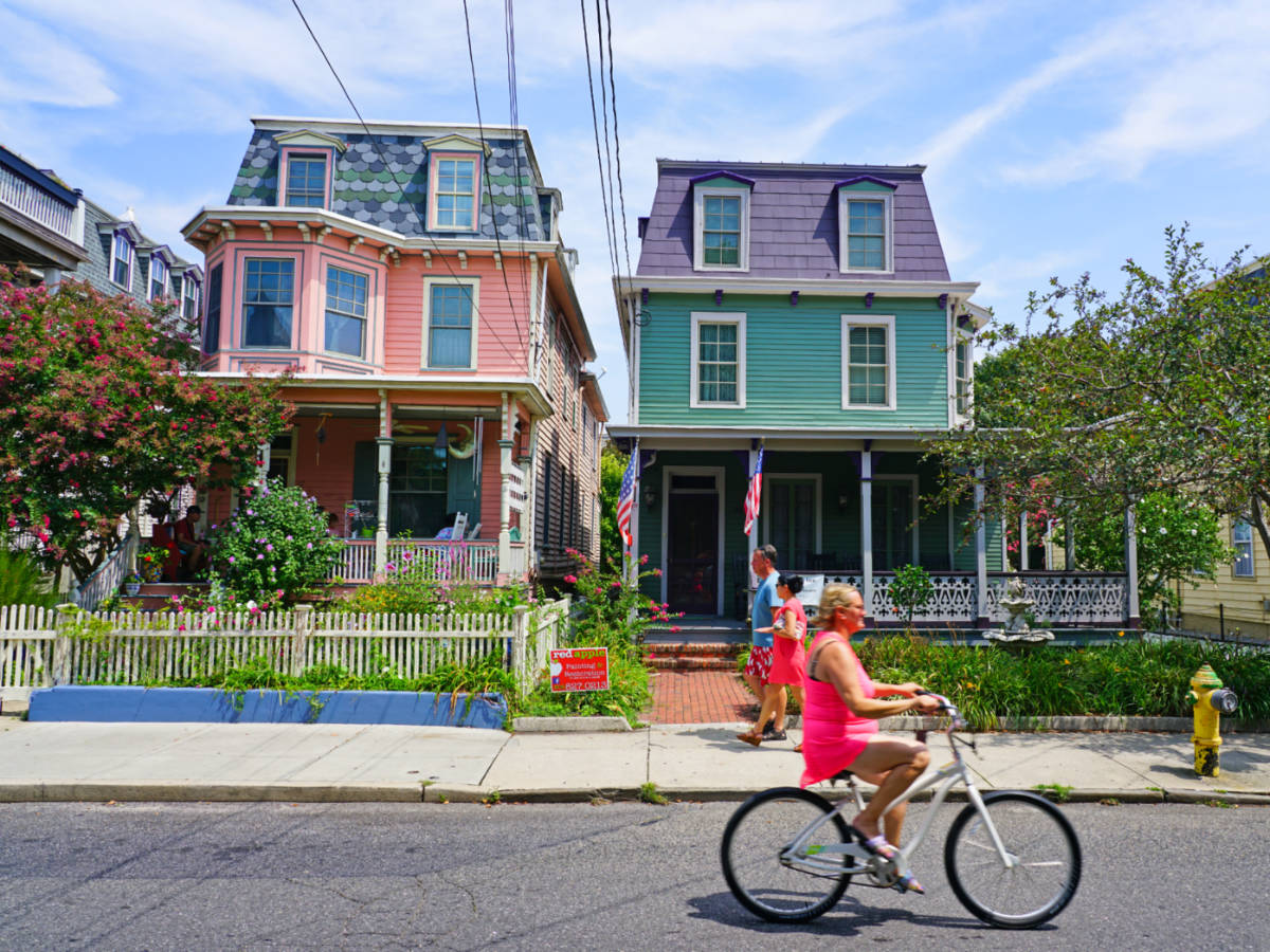 View of the people walking and cycling in front of the colorful Victorian-style homes in Cape May