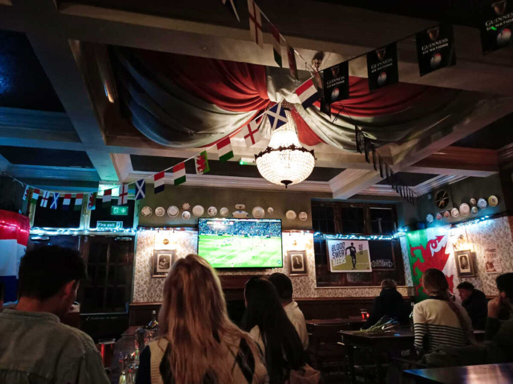 People inside the pub watching the rugby game on the tv screen