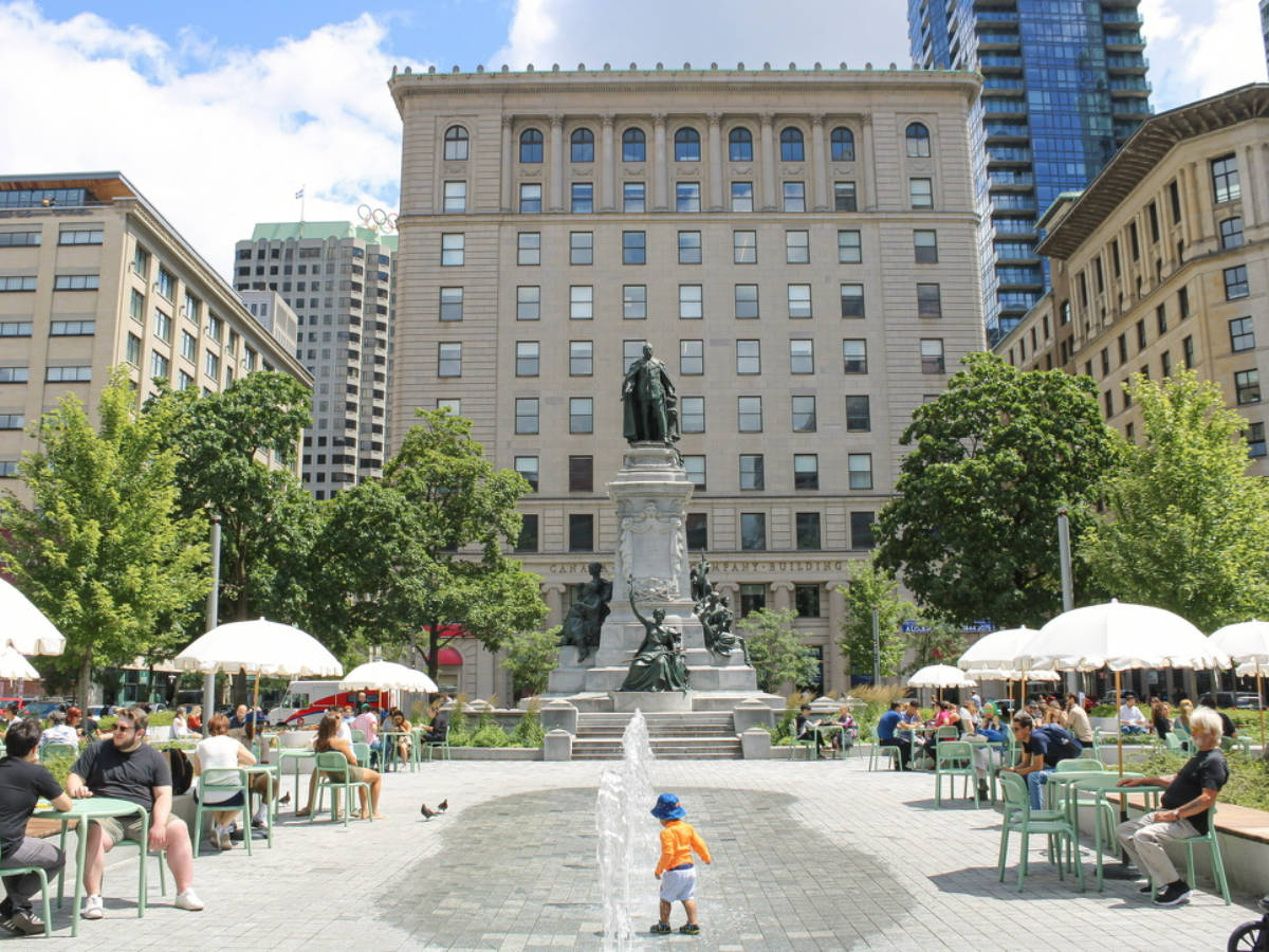 A kid playing with the water fountain and the people relaxing around