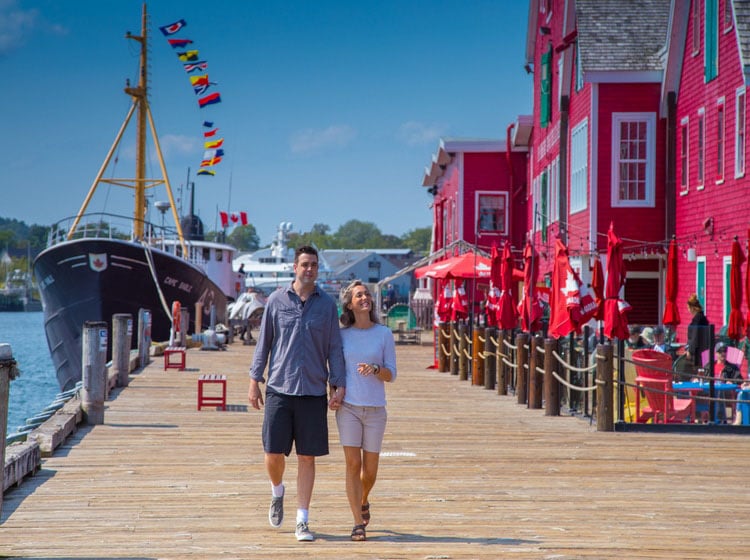 Couple walking along the boardwalk with red buildings in Lunenburg